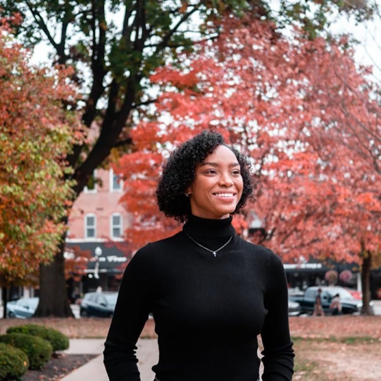Woman in a black turtleneck smiling with autumn foliage in the background.