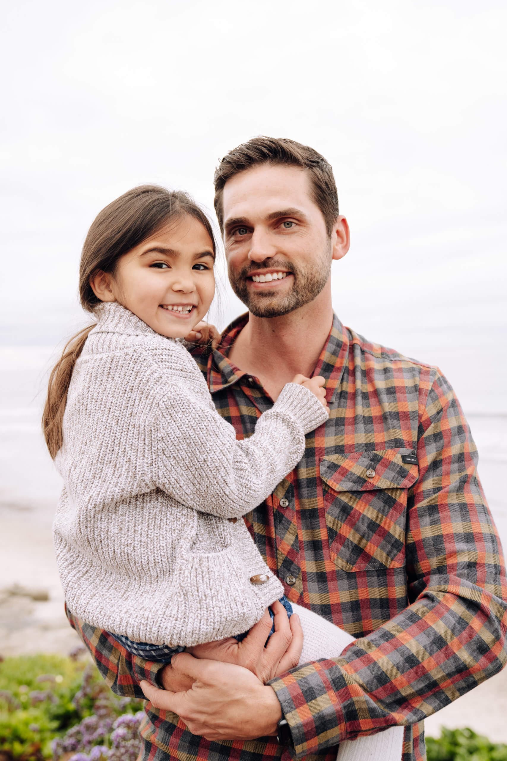 A man holding a young girl in front of a beach setting