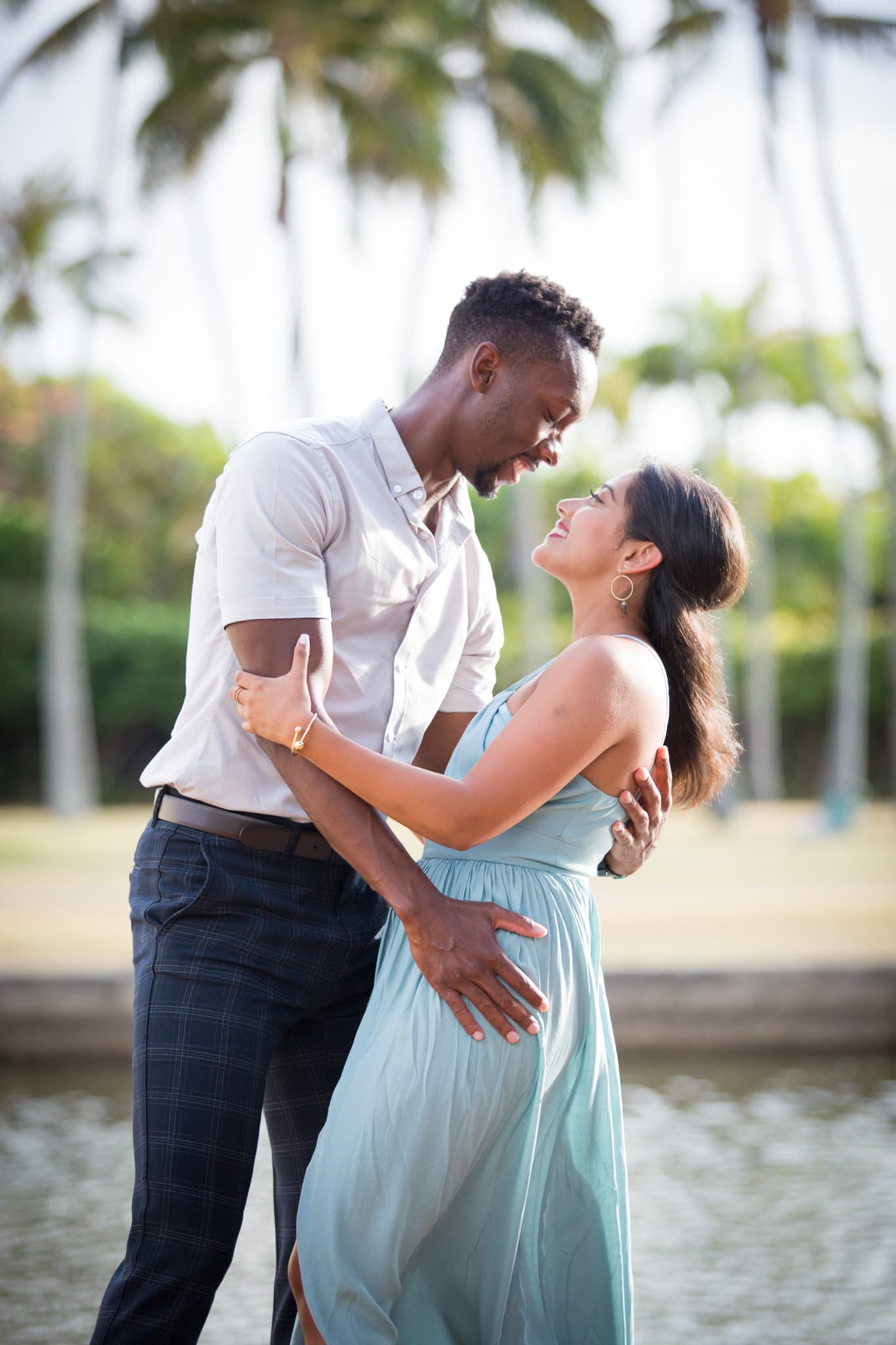 A couple embracing and looking at each other affectionately with palm trees in the background.