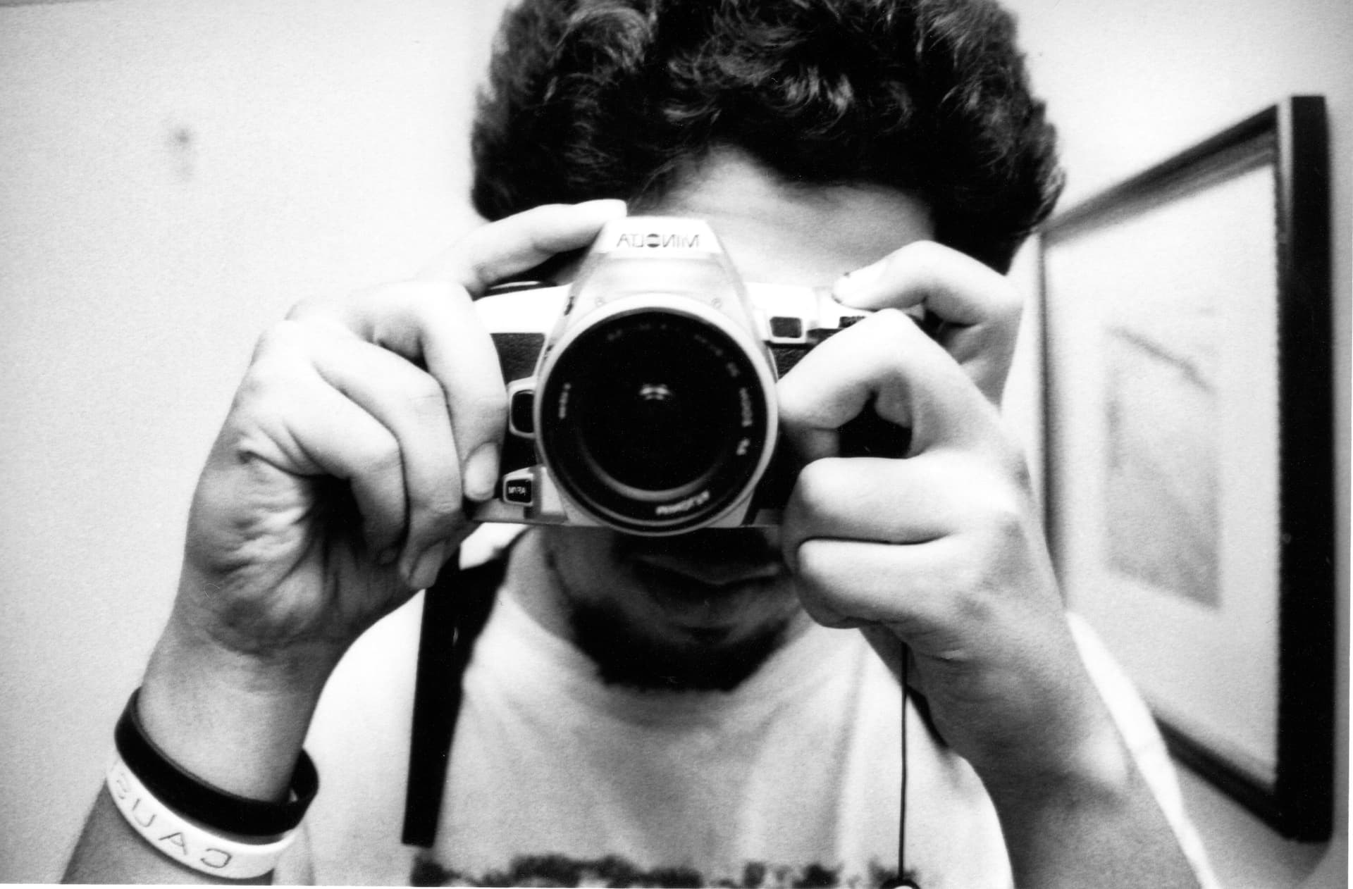Person taking a photo with a vintage camera, obscuring their face.