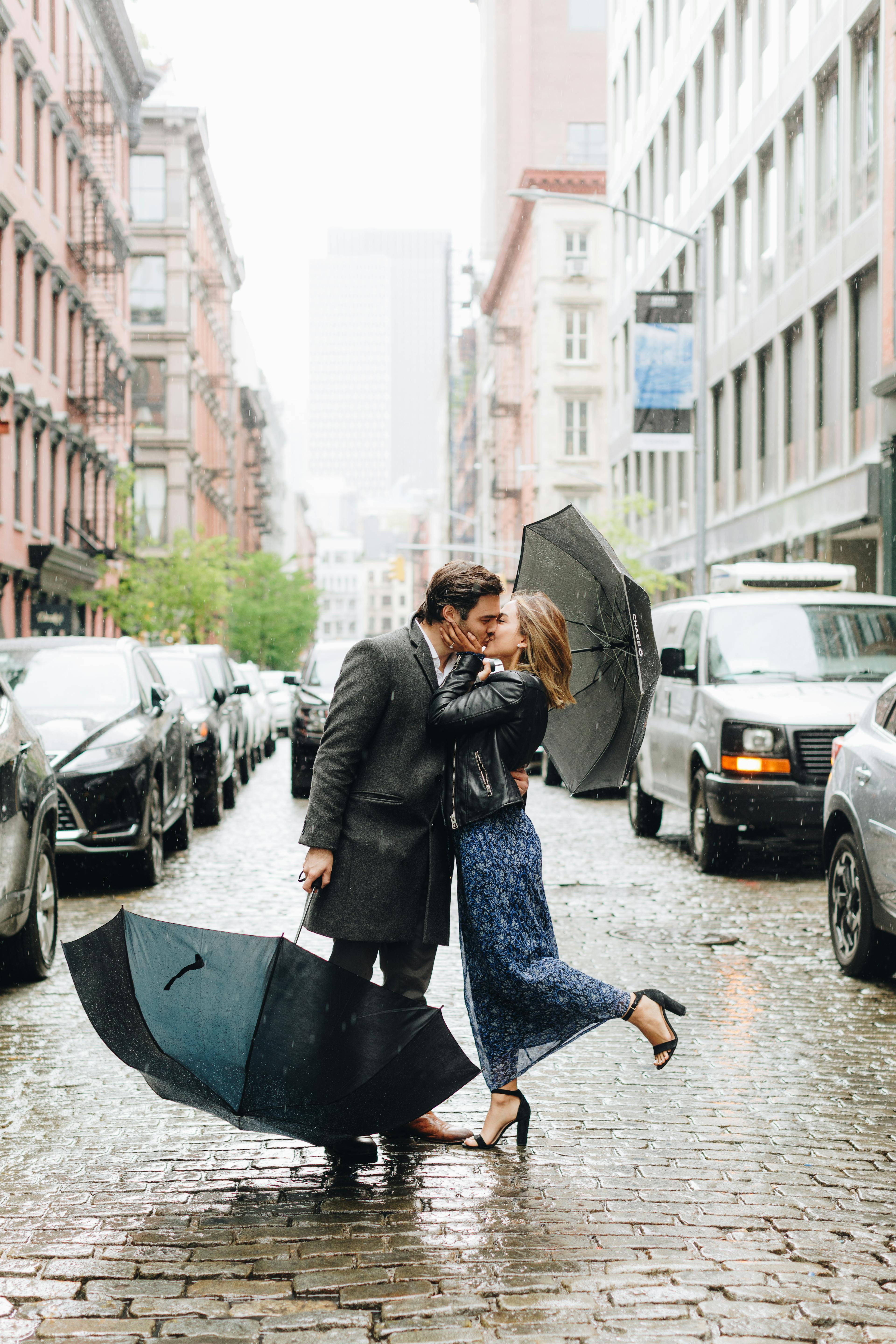 Couple sharing a romantic kiss on a rainy street with umbrellas.