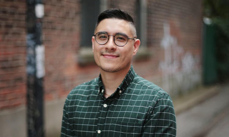 Smiling man with glasses standing in front of a brick wall
