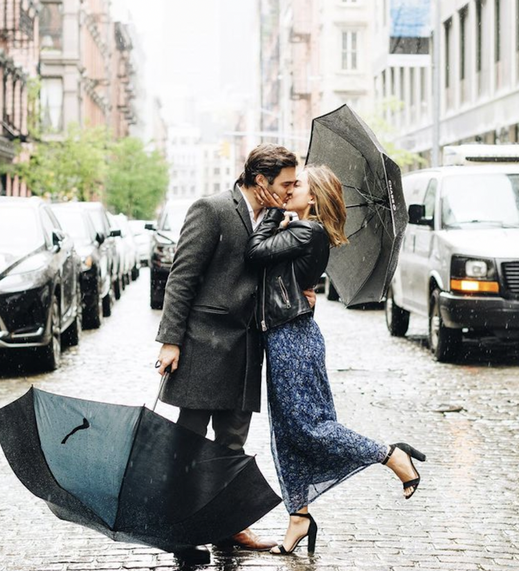 A couple kissing on a rainy city street with overturned umbrellas.