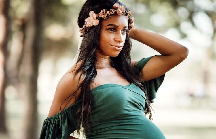 A pregnant woman with floral headband posing with her hand on her hip in a park