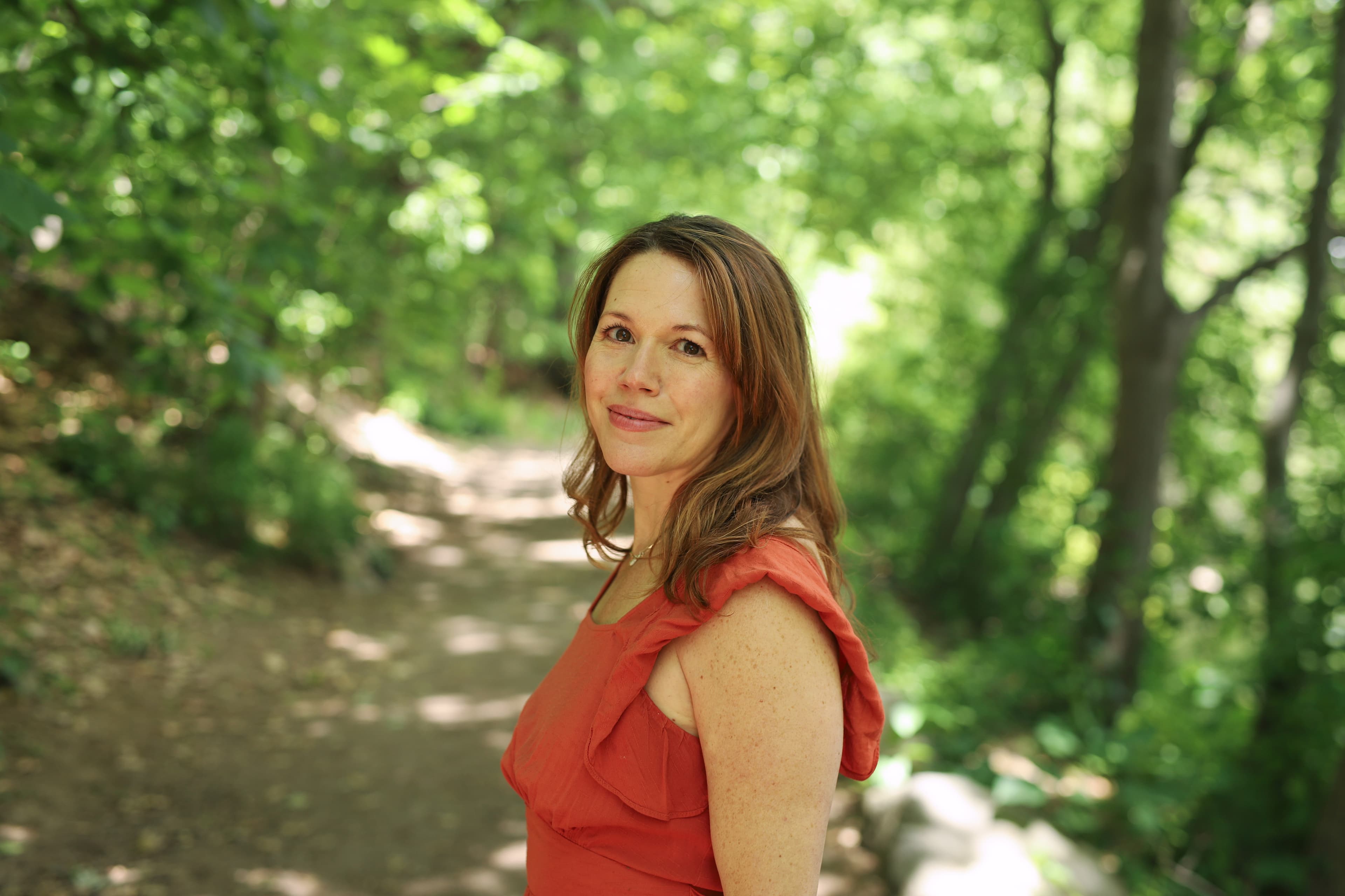 A woman in a red dress looking over her shoulder on a forest path.