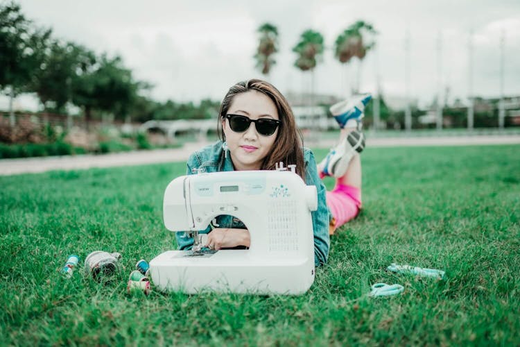 Woman sewing on a portable sewing machine outdoors on a grass field