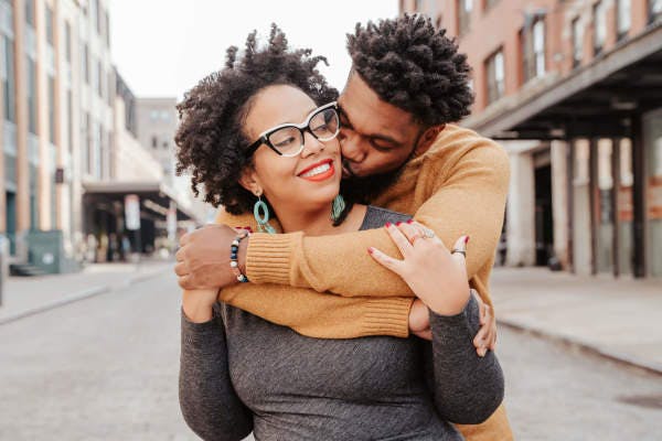 Man kissing a smiling woman on the cheek on an urban street.