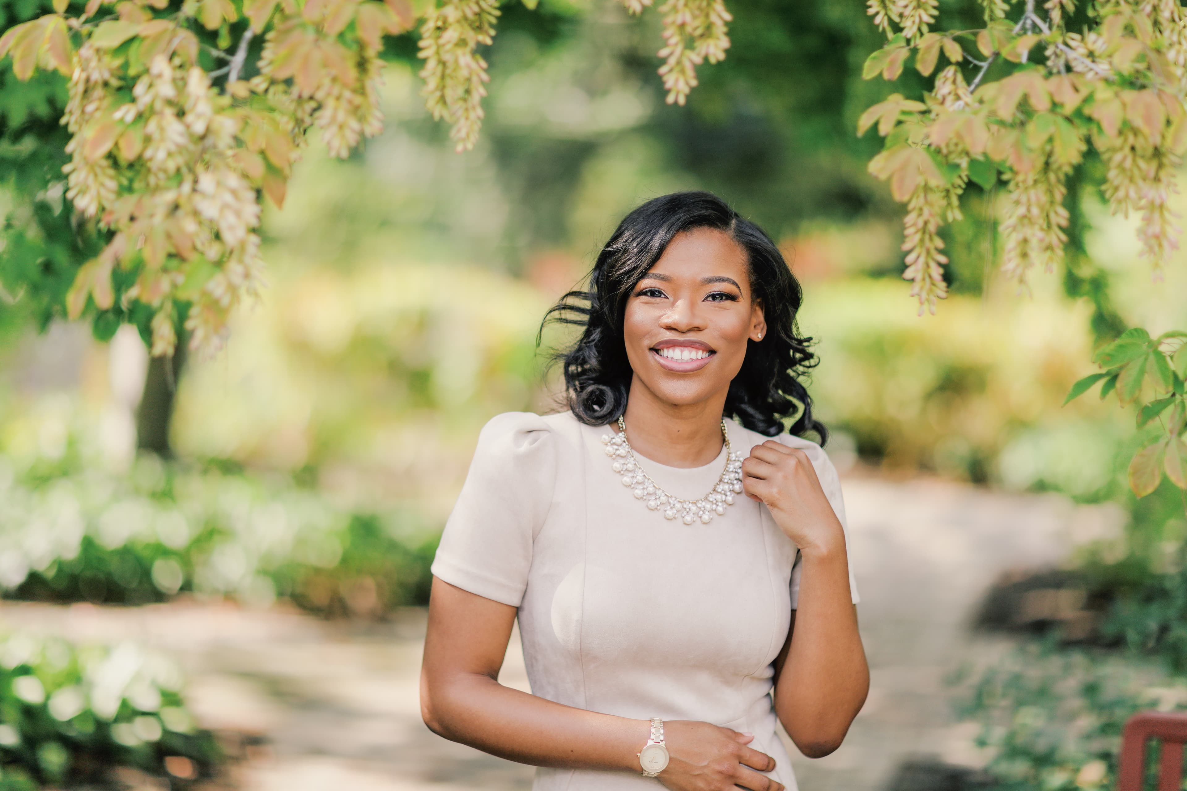 Smiling woman with pearl necklace standing in a garden.