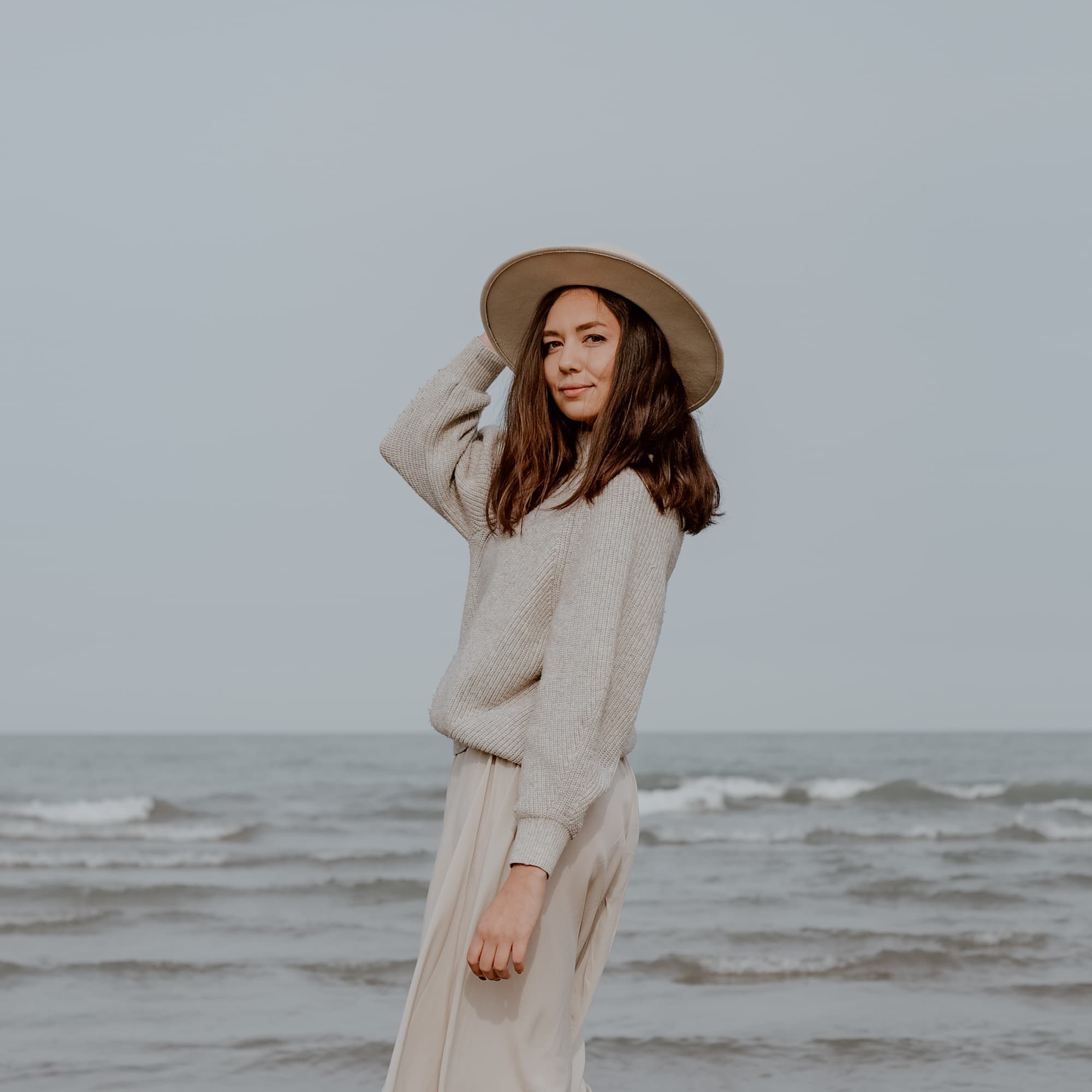 "Woman in a wide-brimmed hat standing on the beach with the ocean in the background."