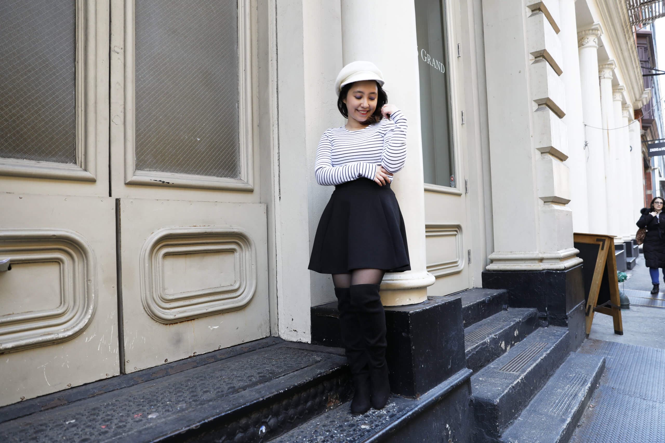 A person standing on steps outside a building, smiling and adjusting a white hat