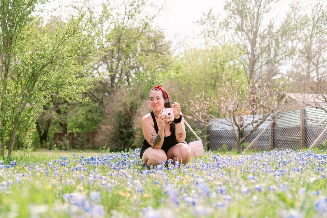 Person with a camera sitting in a flower field.