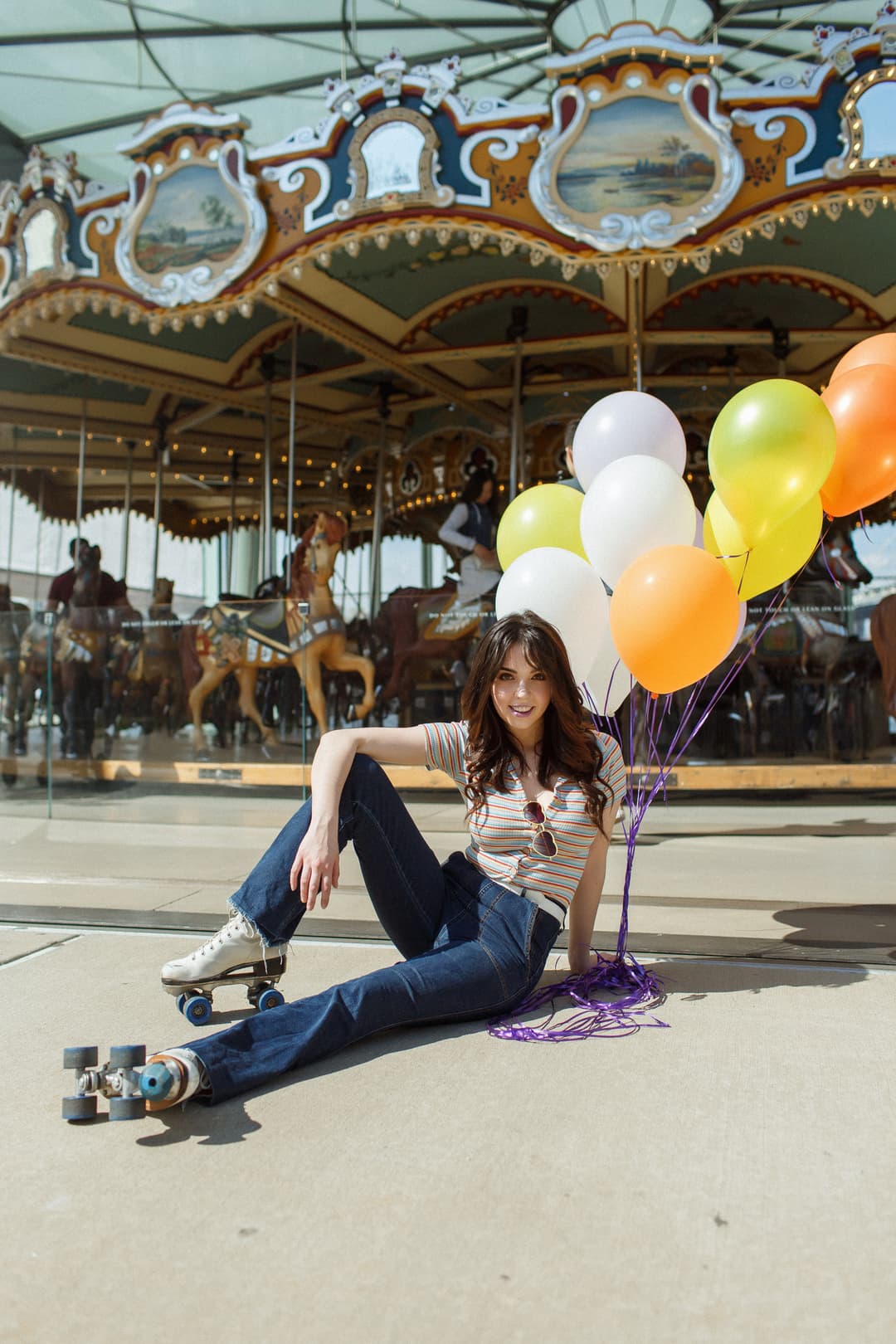 Woman in roller skates sitting in front of a carousel holding orange, yellow, and white balloons, captured during her Shoott session.
