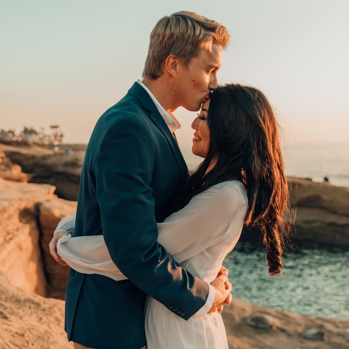 A couple embracing by the seaside at sunset.