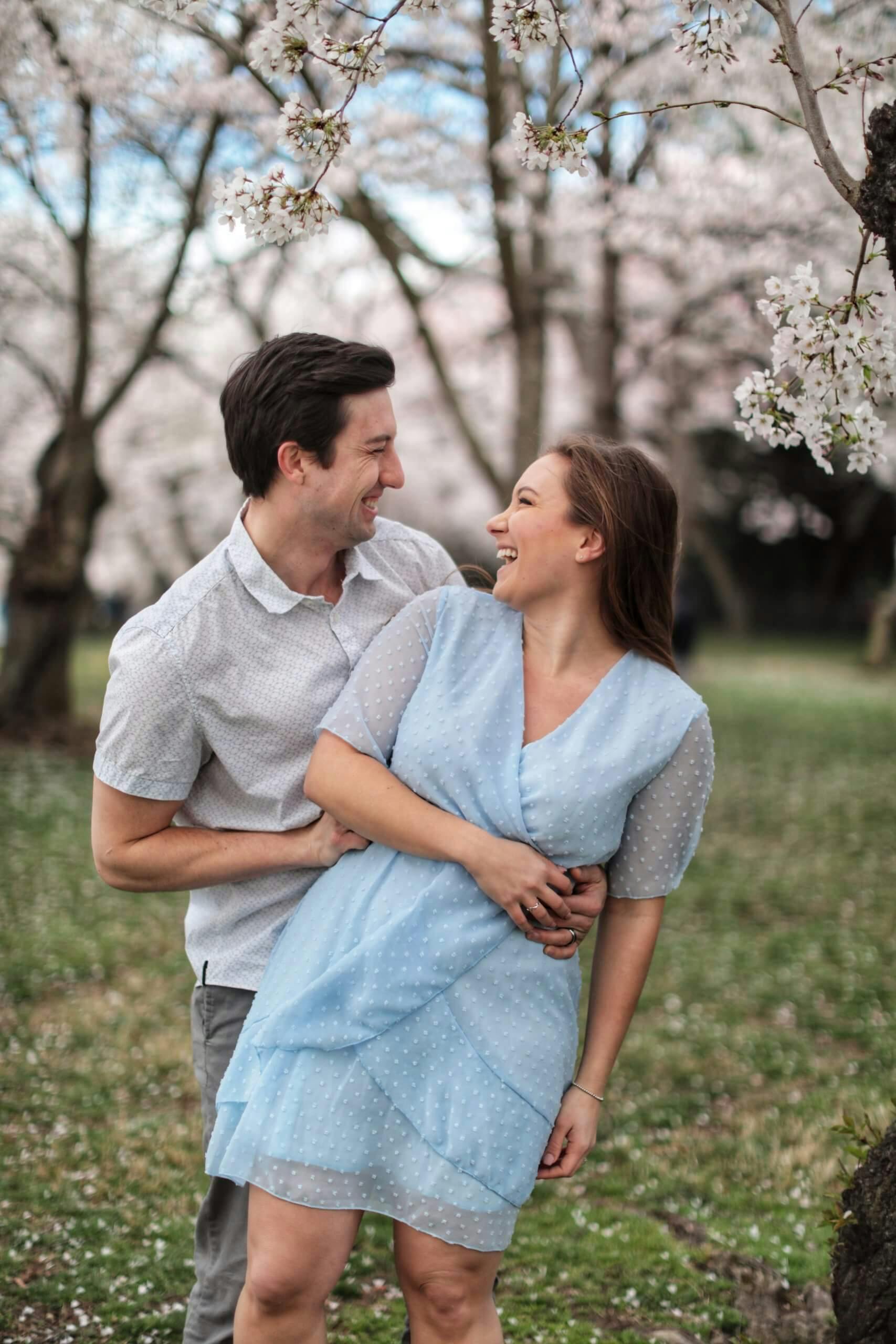 A couple smiling and embracing each other in a field filled with cherry blossoms.