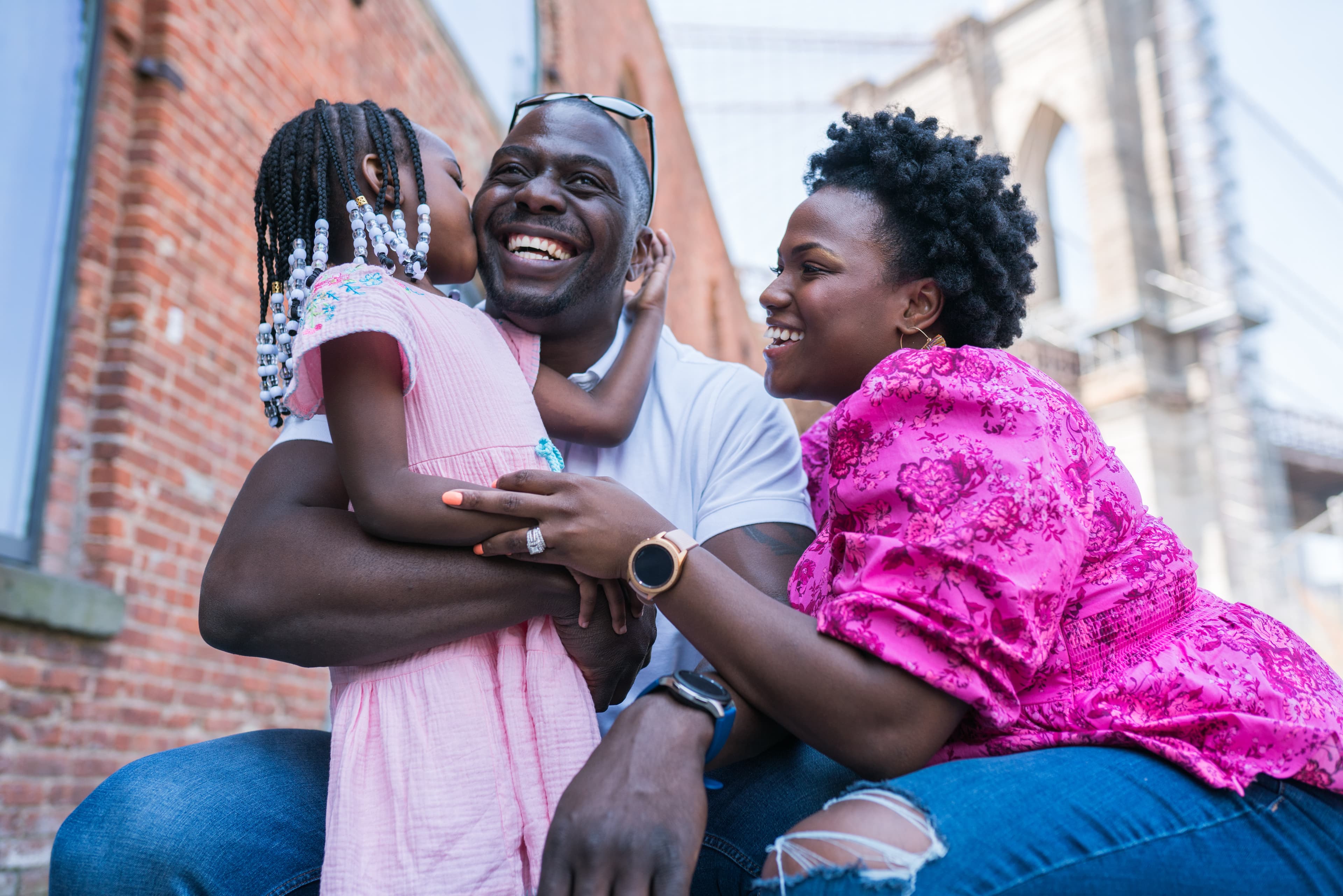 A joyful family moment with a father, mother, and daughter hugging and laughing together outdoors