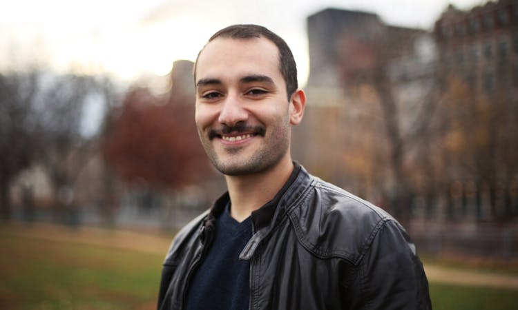 Man in a leather jacket smiling in an urban park at dusk