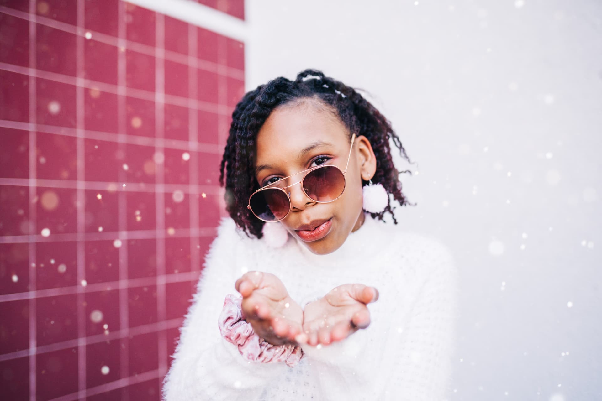 Young girl with sunglasses blowing snowflakes from her hands.