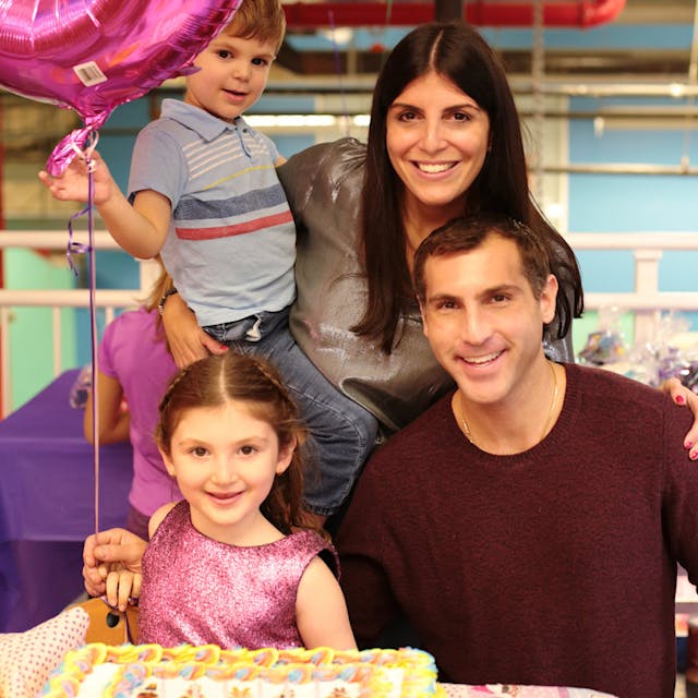 Family with two adults and three children smiling with a balloon and birthday cake