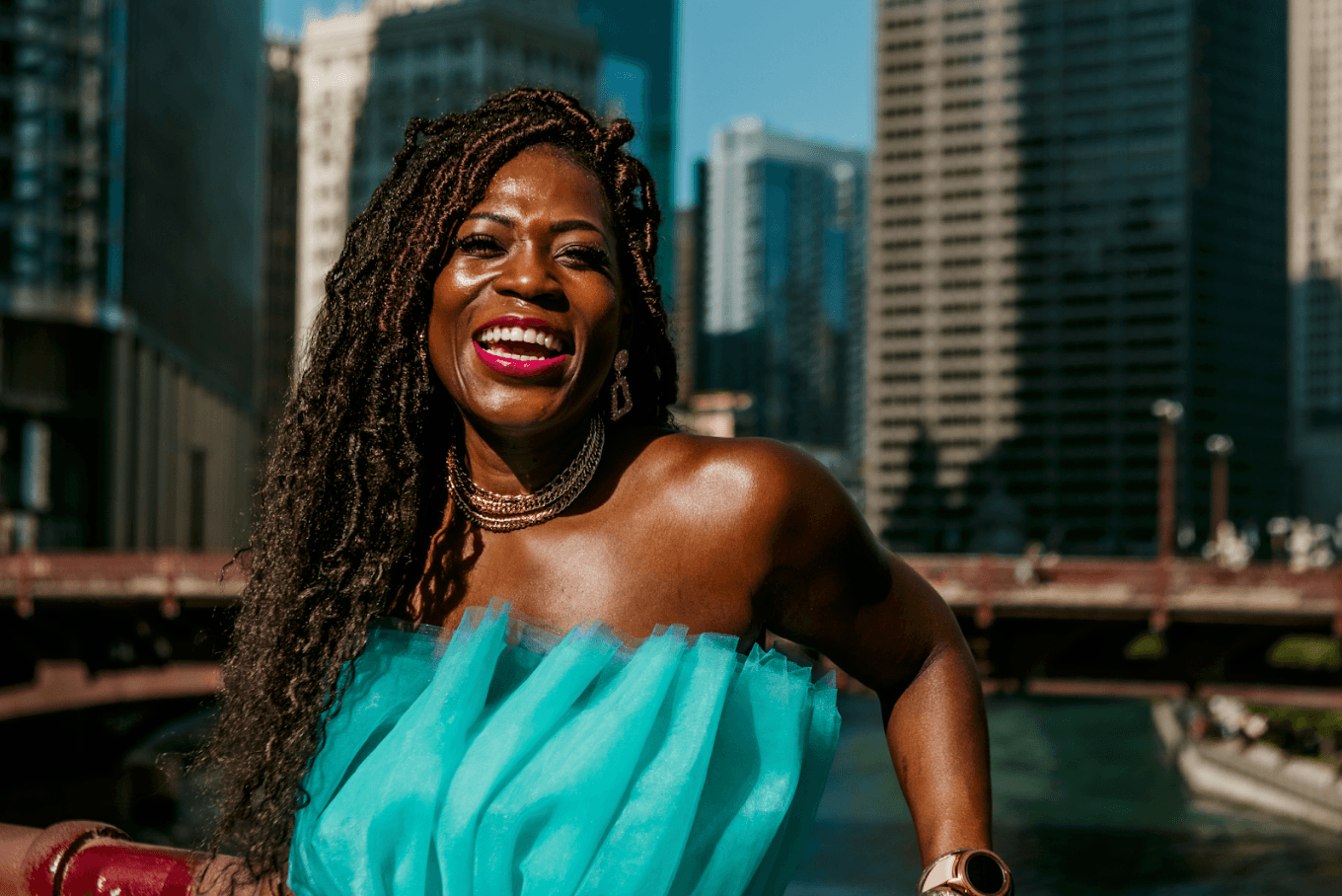 Woman laughing in a turquoise dress with gold jewelry and city skyline behind her during free professional lifestyle photo session with Shoott in Houston
