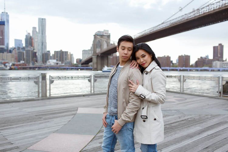 A young couple embracing with a bridge and city skyline in the background.