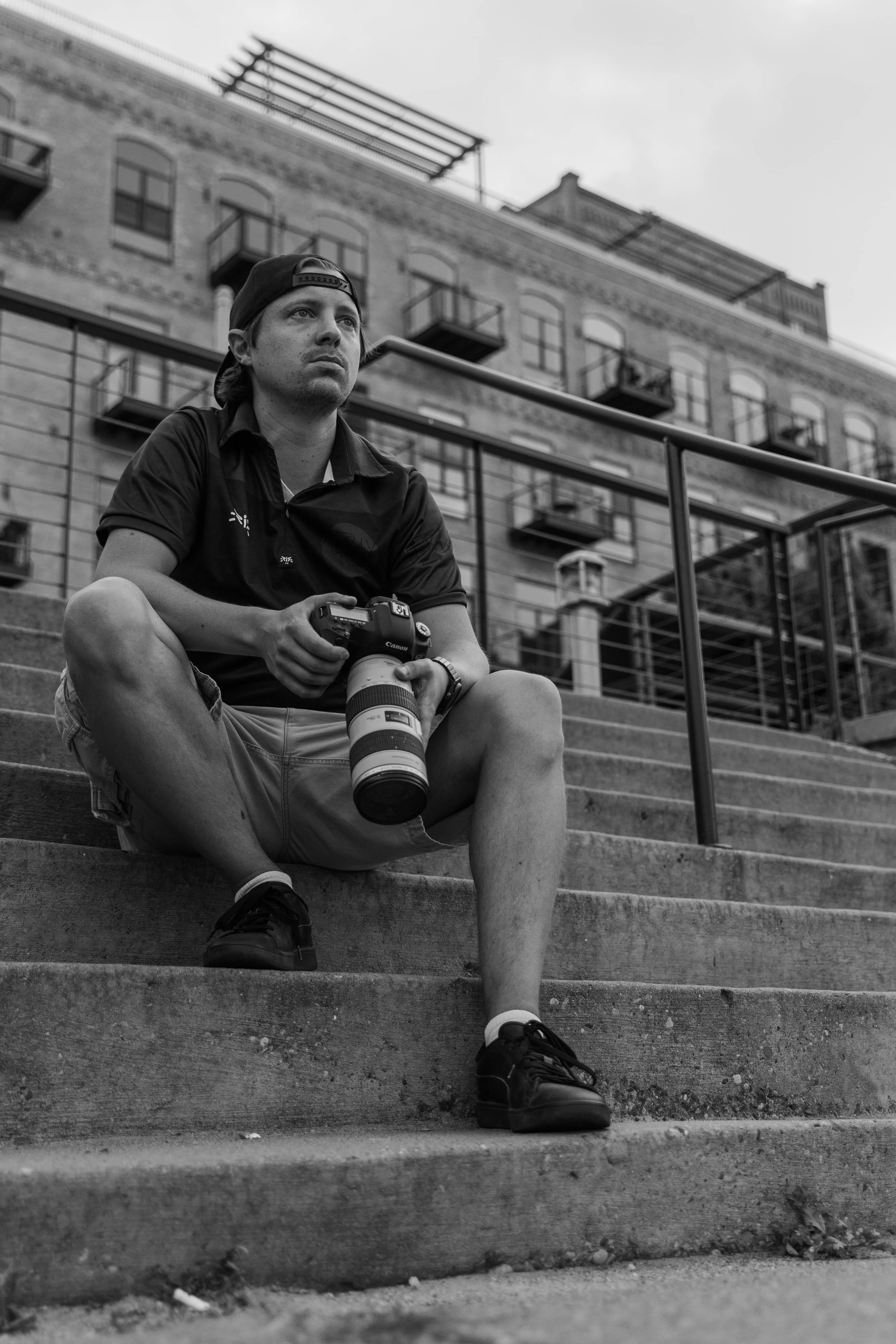 A photographer sitting on urban steps holding a camera.