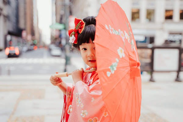 Young child holding an orange umbrella and wearing traditional Asian attire.