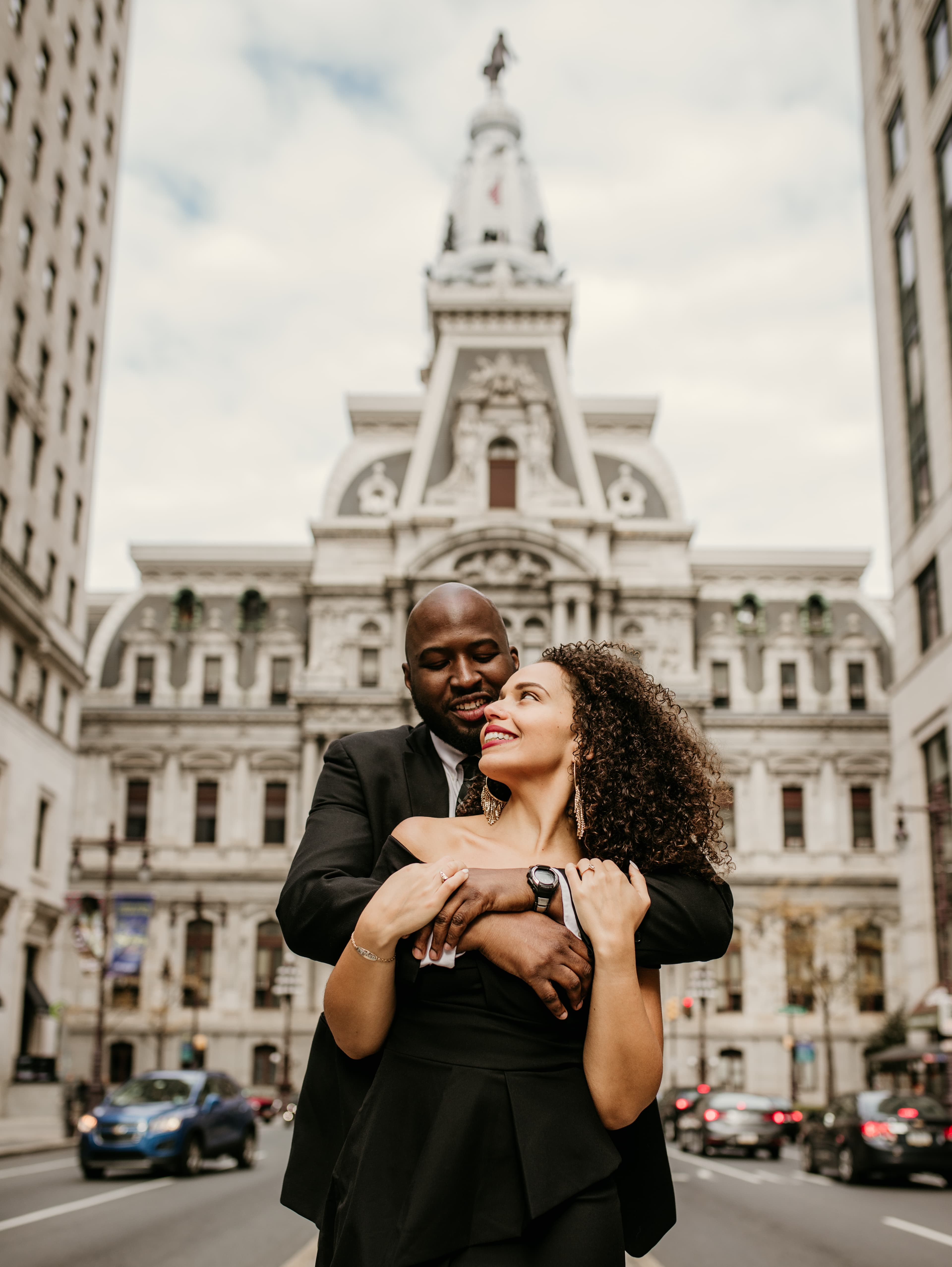 A couple embracing in front of a historic building on a city street.