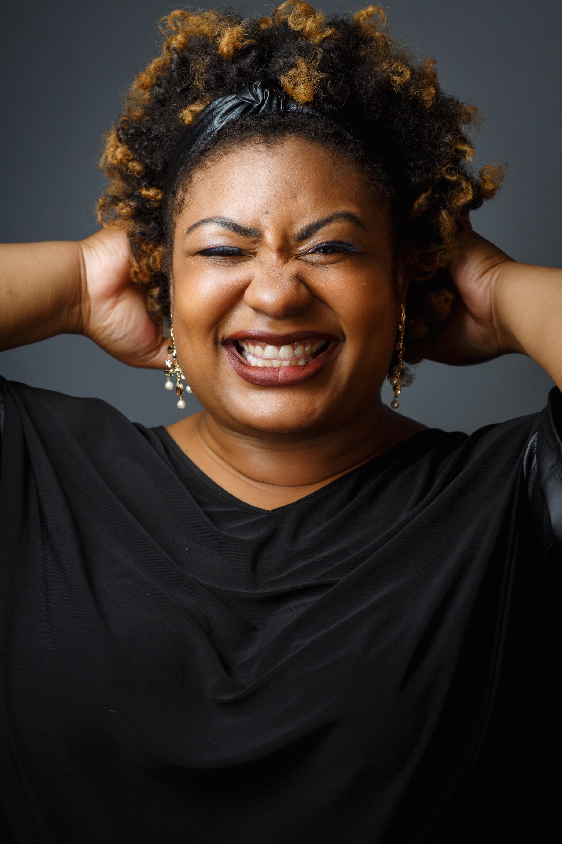 Woman laughing with hands on her head against a gray background.
