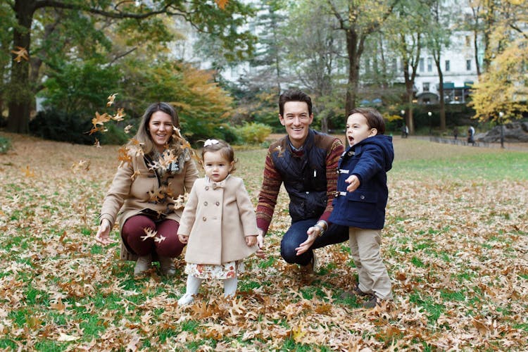 Family of four playing with falling leaves in a park during autumn