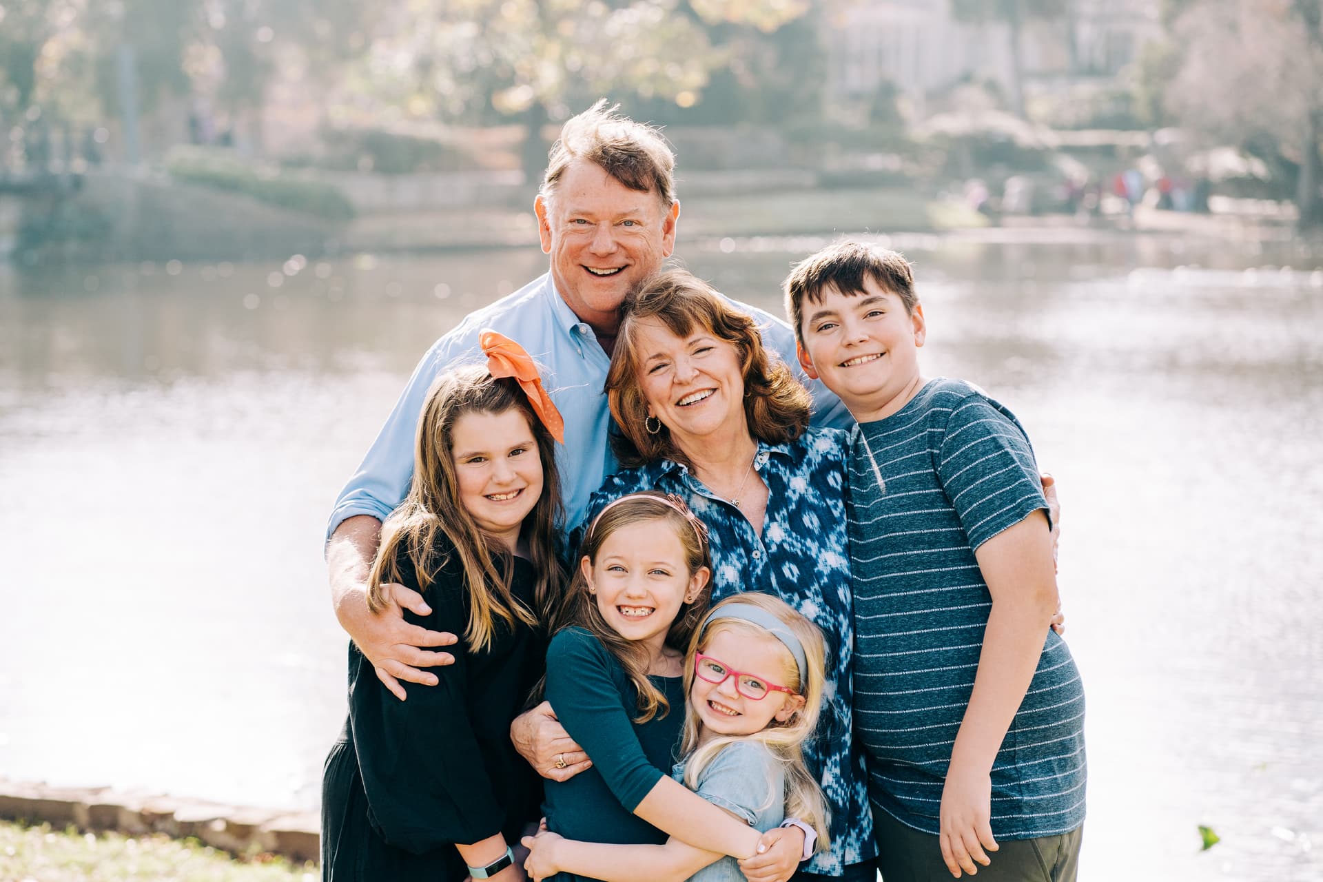 A happy family with two adults and three children posing with a smile in front of a body of water.