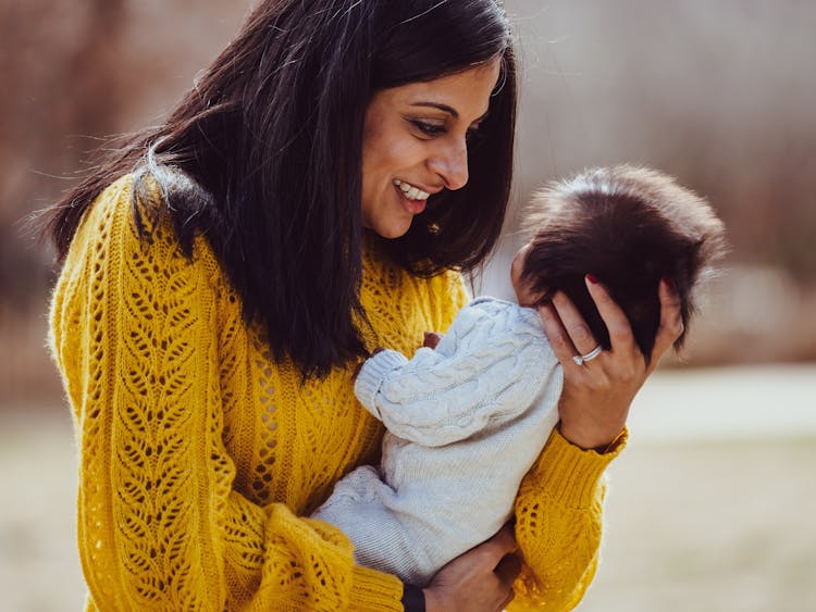 Smiling woman in a yellow sweater holding and looking affectionately at a baby.