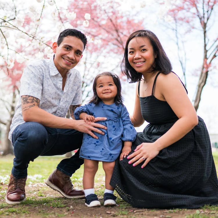 Family with a young child smiling under cherry blossom trees.