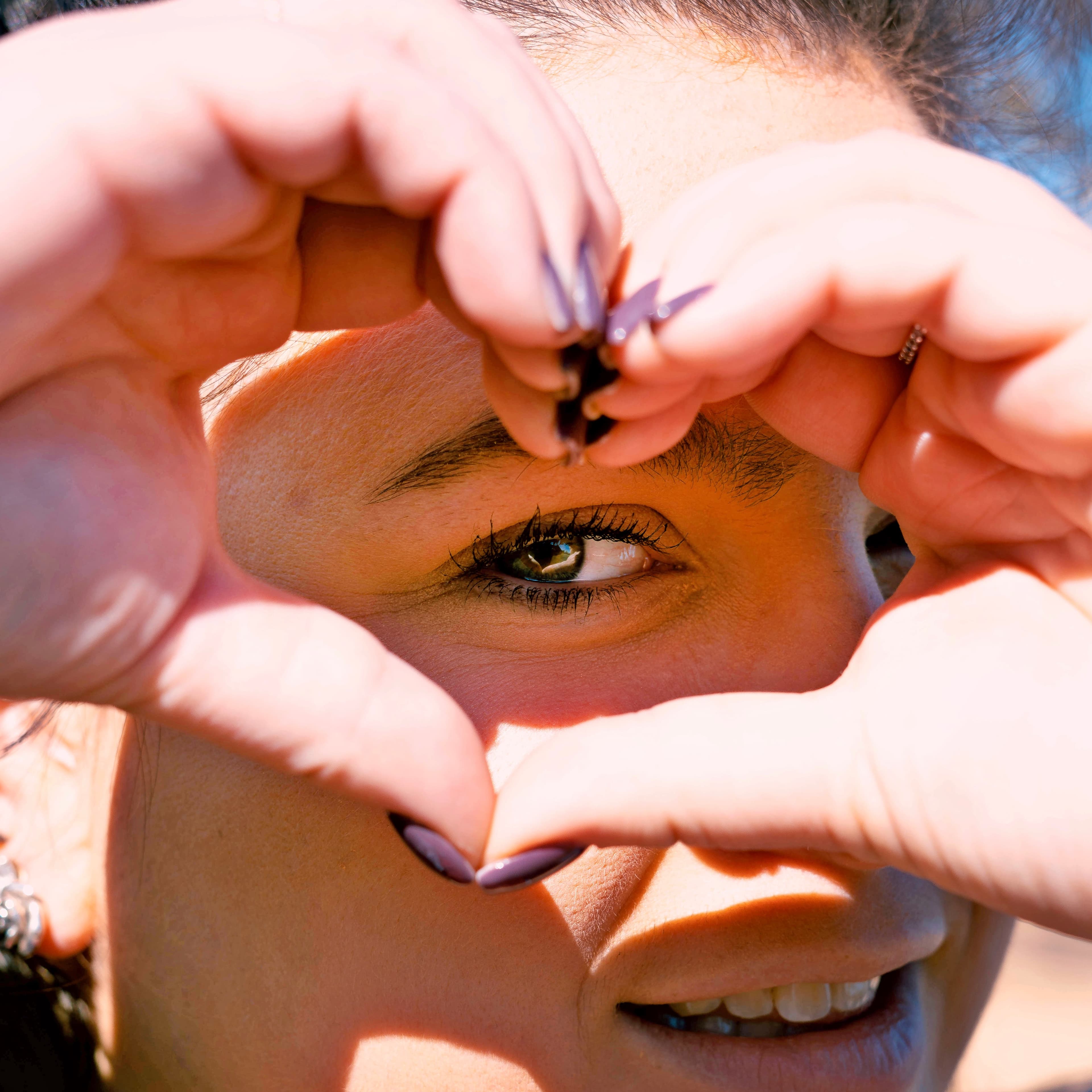 A woman making a heart shape with her hands around her eye.