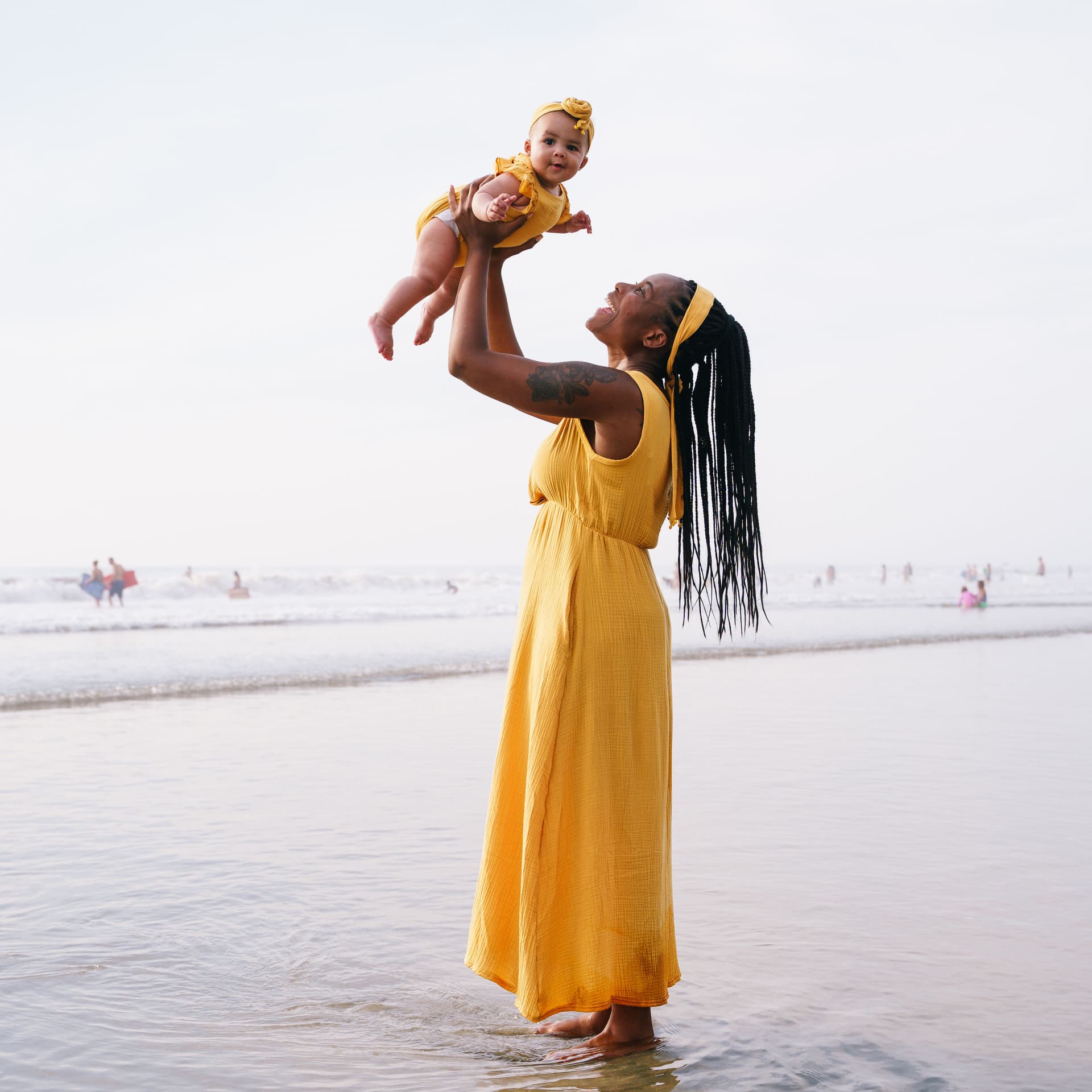 Mother and baby in matching yellow outfits pose on the beach for their free outdoor photoshoot