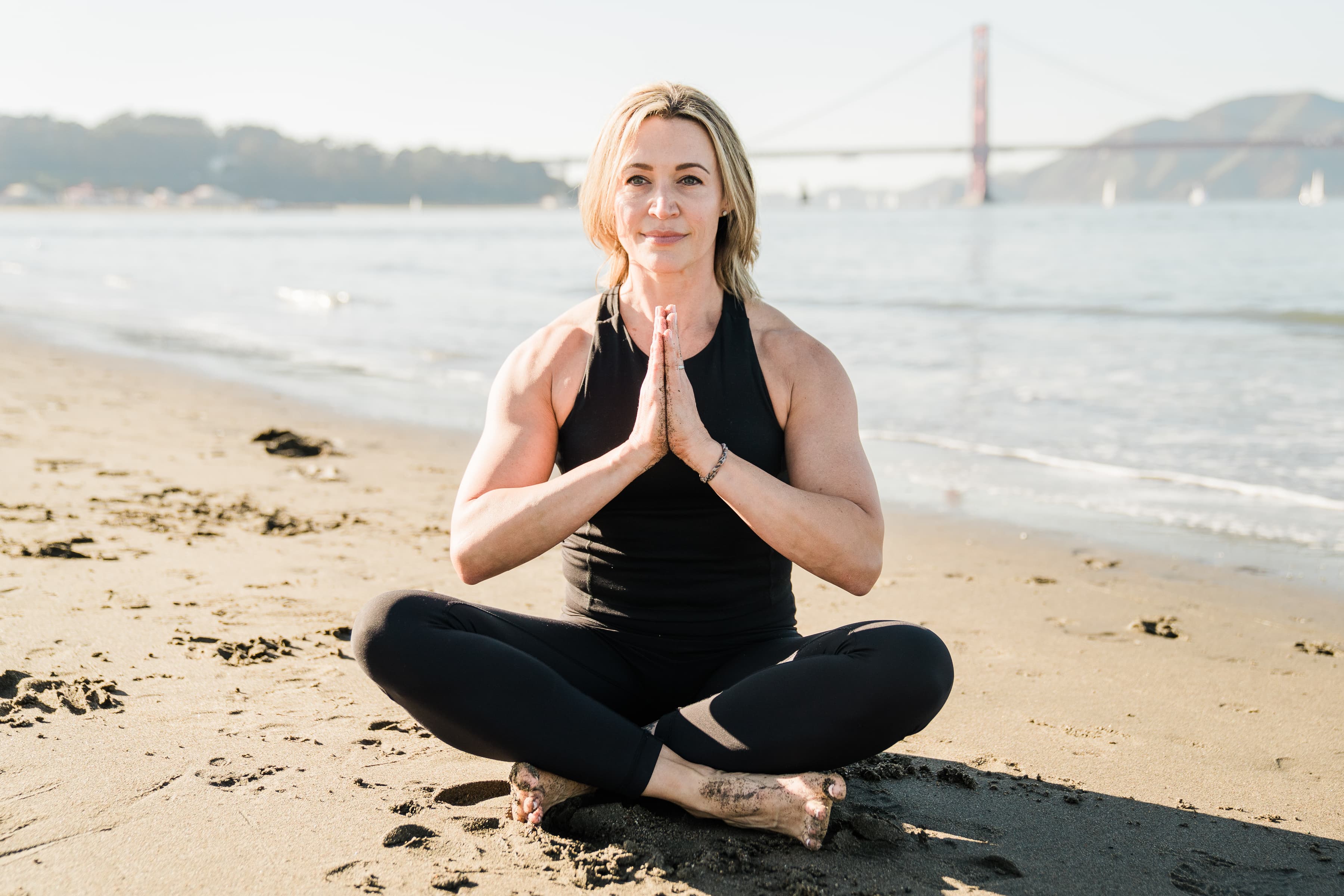 Woman practicing yoga on the beach with the Golden Gate Bridge in the background.