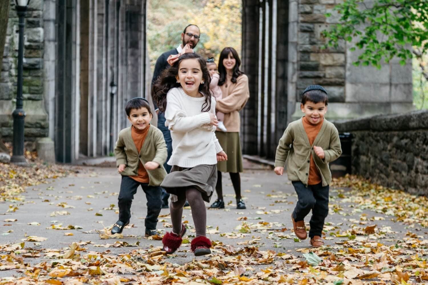 Three children running towards the camera with two adults behind them