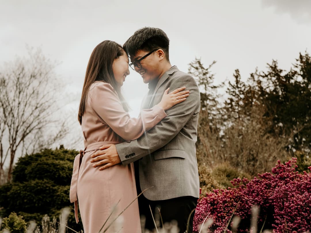 A couple touches foreheads lovingly surrounded by flowers.