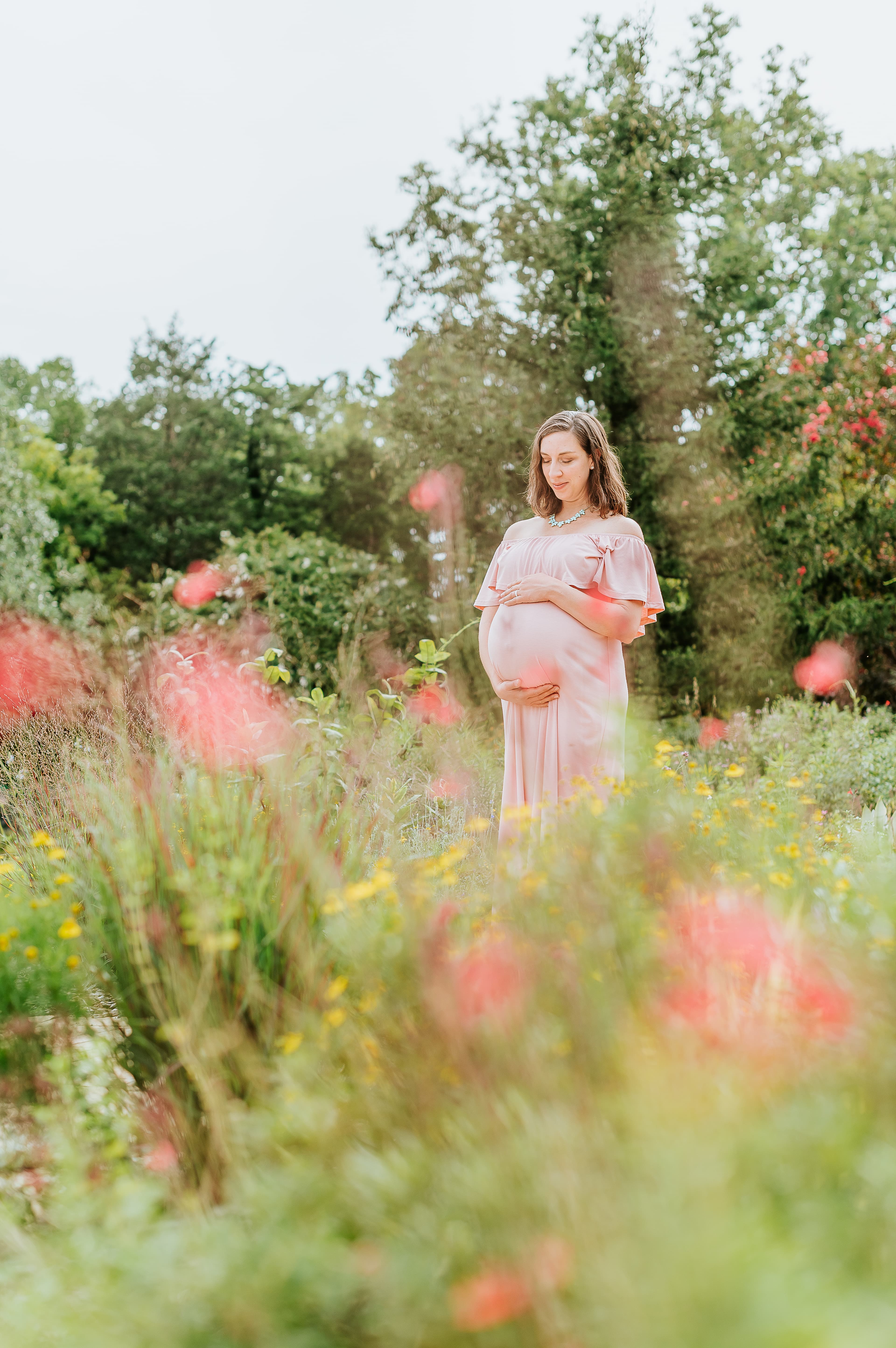 Pregnant woman standing in a field of flowers.