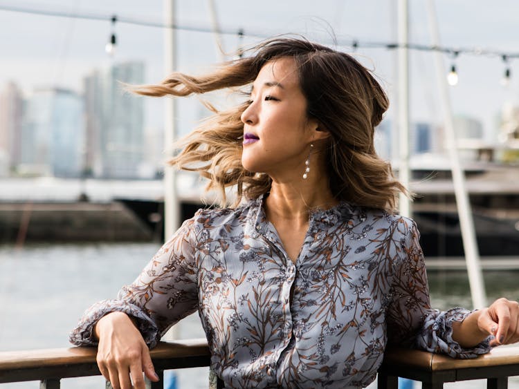 Woman in a patterned blouse with her hair blowing in the wind by the waterfront.