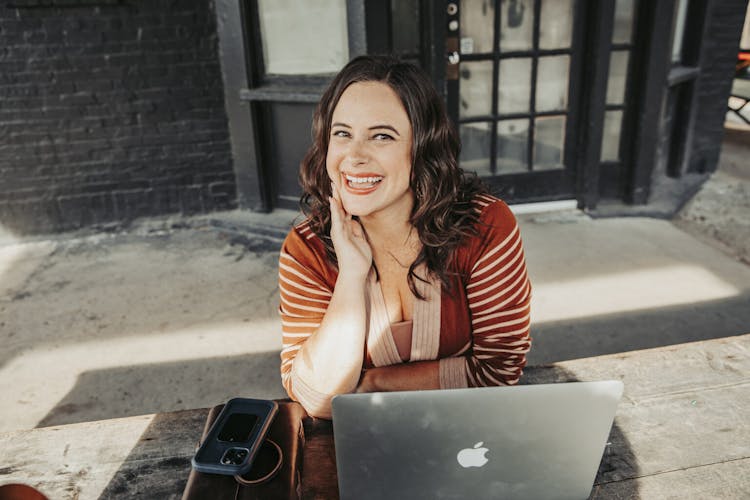 Woman smiling while sitting at a table with a laptop and smartphone.