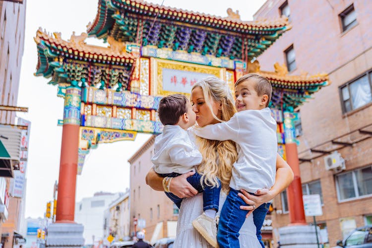 A woman hugging two children in front of a colorful Chinese archway.