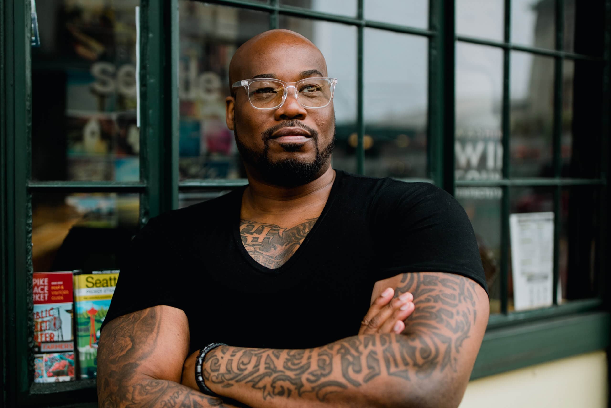 Confident man with tattoos standing with arms crossed in front of a window