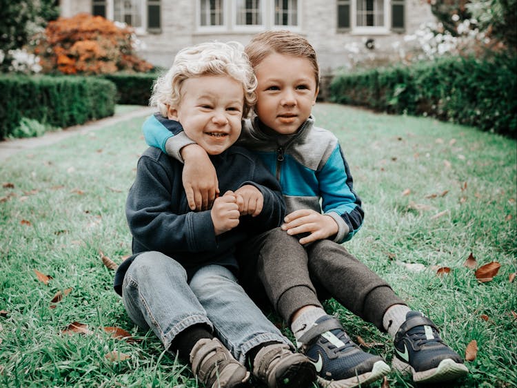 Two young boys smiling and hugging while sitting on grass