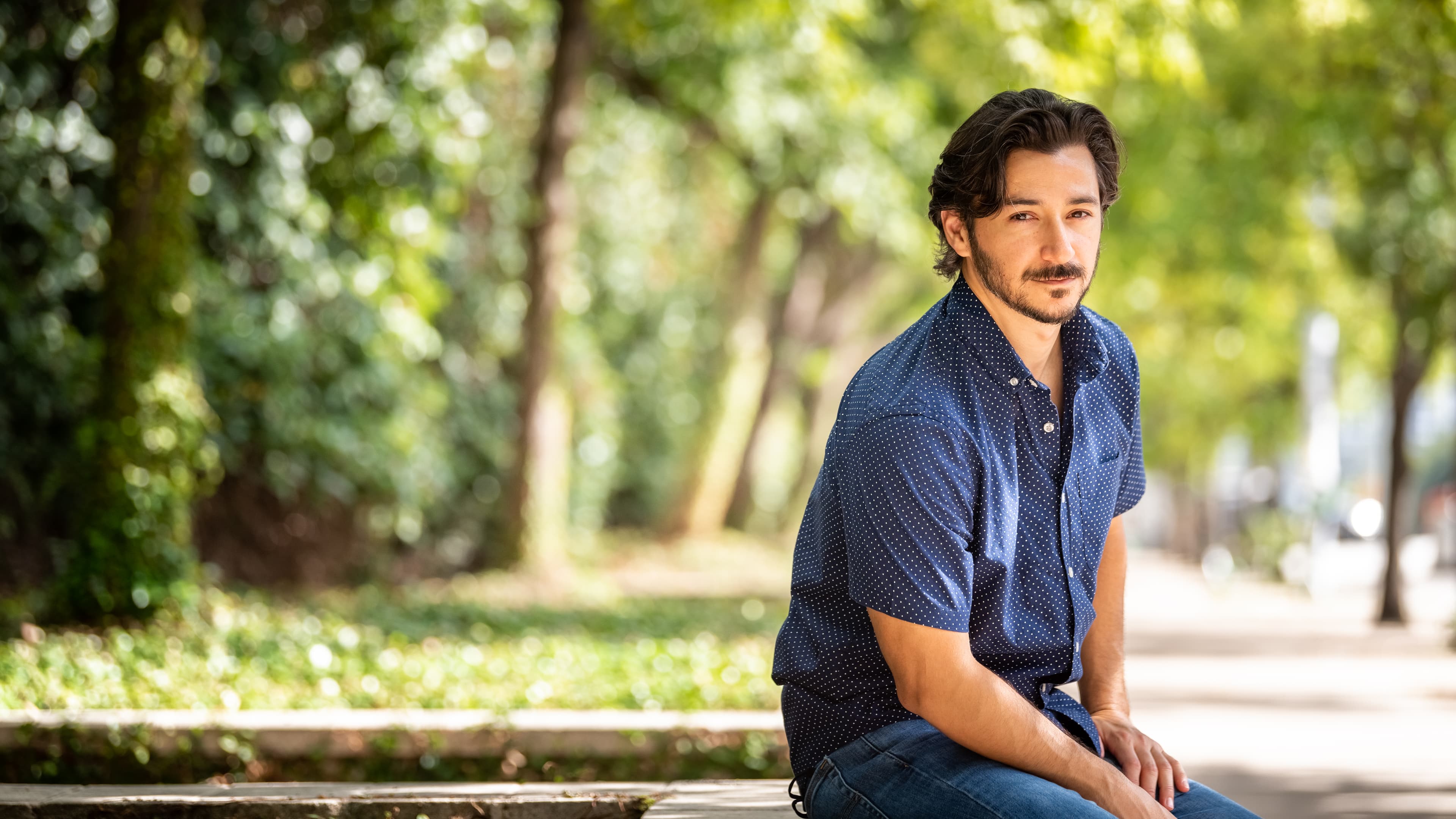 Man sitting on a park bench with trees in the background.