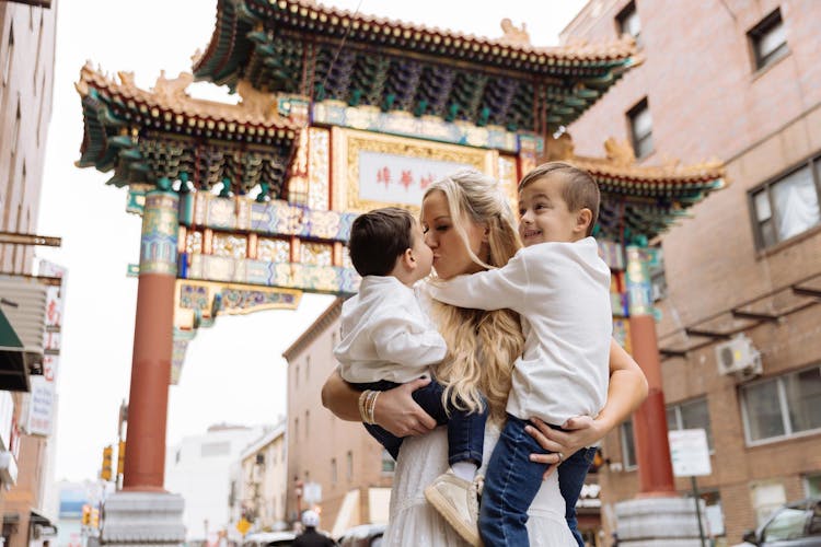 A woman holding two young children under an ornate, traditional Chinese gate.