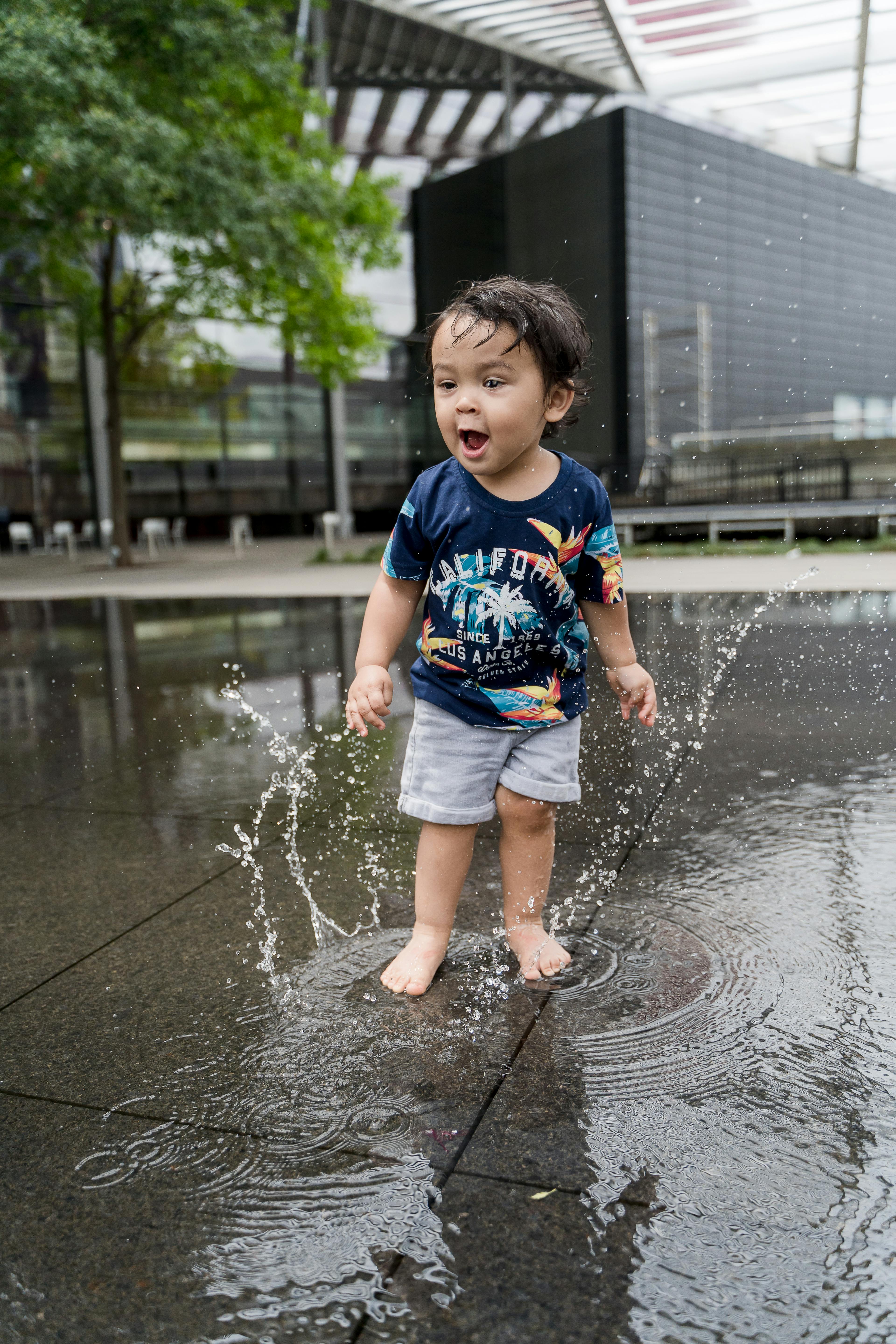A joyful toddler playing in water on a wet urban surface.