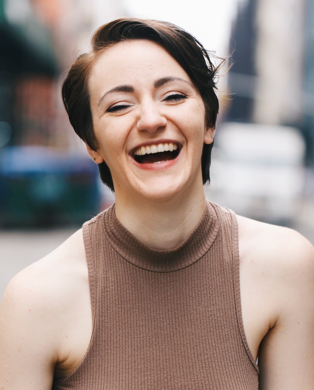 A joyful woman with short hair laughing in an urban setting.