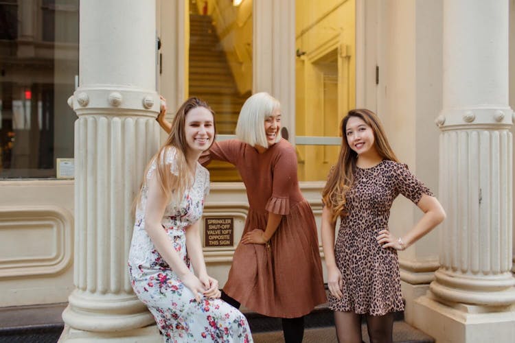 Three young women smiling and posing on a city street.