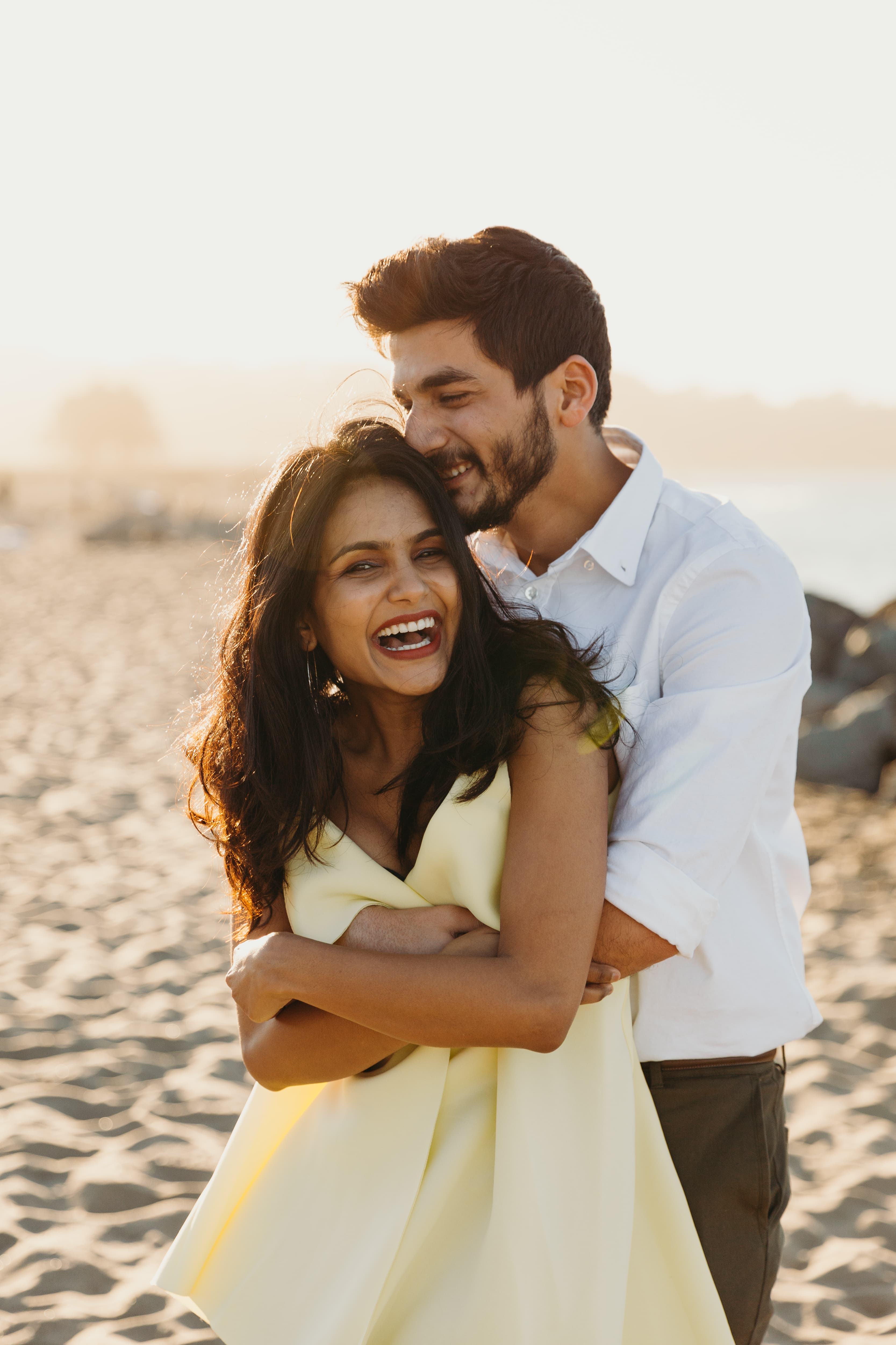 A happy couple embracing and laughing on the beach at sunset.