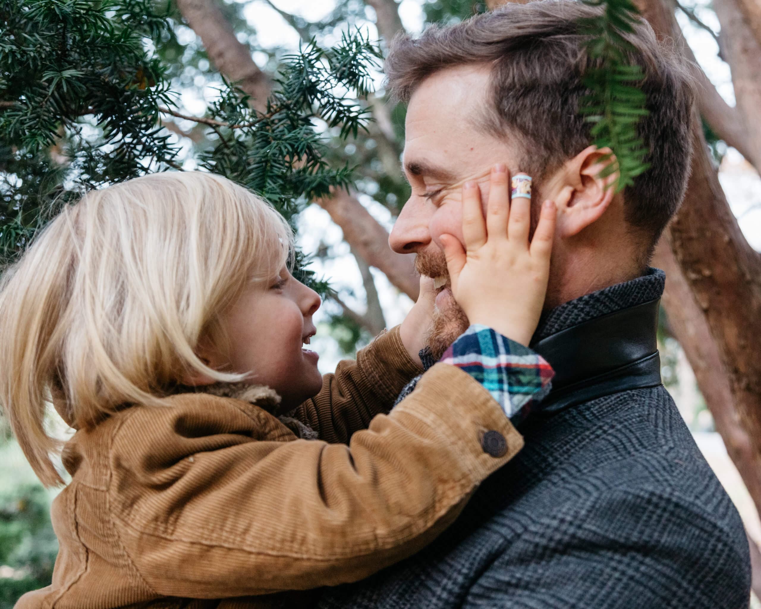 A child placing their hands on a man's face, both smiling in a close embrace